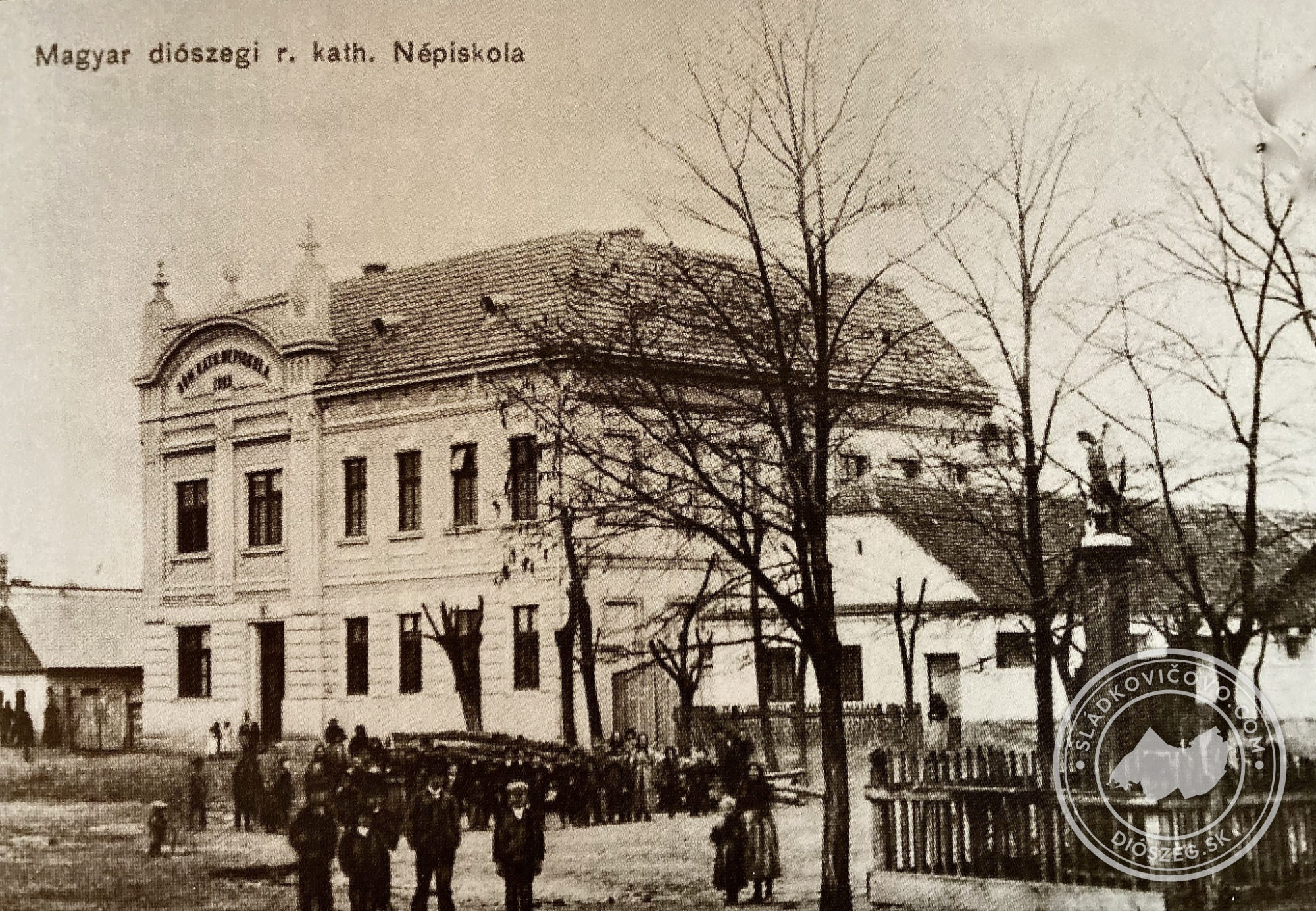 Az 1910-es képeslapon a Római katolikus népiskola – Rímsko katolícka ľudová škola 1909-ben épült új épülete látható a Fő utca szomszédos házaival.